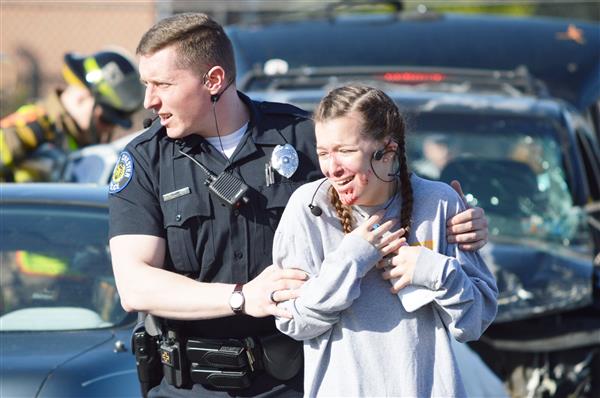 Emergency personnel lead a student actor away from the accident scene 